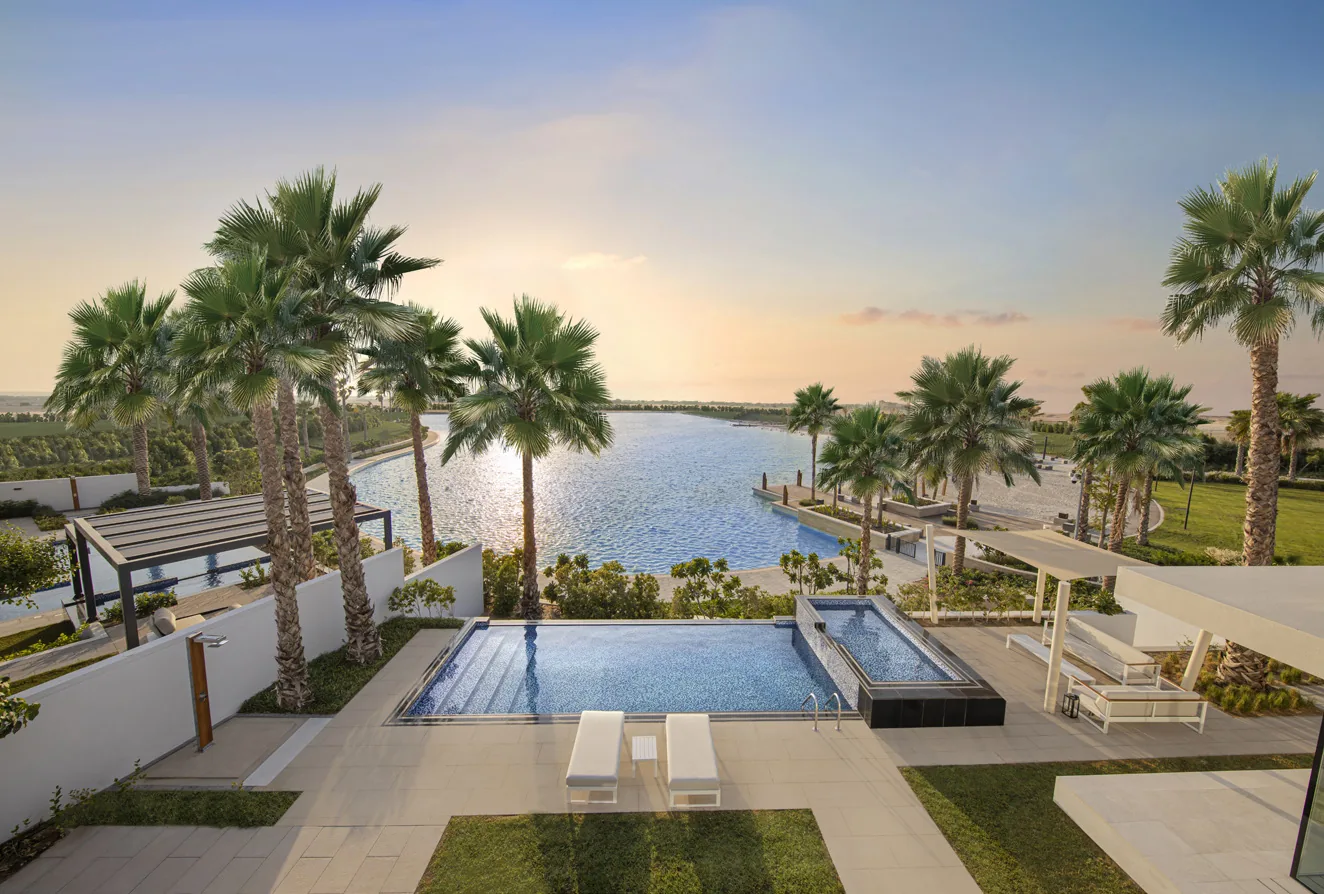 Pool deck beside the recreational lagoon at Tilal Al Ghaf, lined with palms and sun loungers at sunset